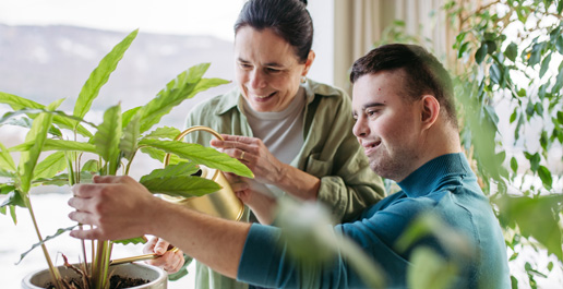 Cliënt met downsyndroom verzorgt een plant samen met een begeleider