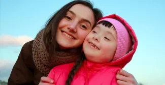 jonge vrouw samen met kind met syndroom van down, ze hebben de hoofden tegen elkaar