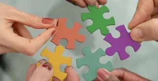 vijf handen die allemaal een puzzelstukje vast houden in een verschillende kleur