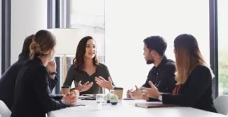 Vier professionals in gesprek rond een tafel, waarbij een vrouw aan het woord is en de anderen aandachtig luisteren.