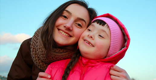 jonge vrouw samen met kind met syndroom van down, ze hebben de hoofden tegen elkaar