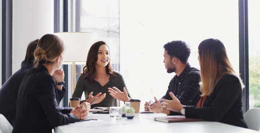 Vier professionals in gesprek rond een tafel, waarbij een vrouw aan het woord is en de anderen aandachtig luisteren.
