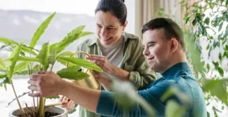 Cliënt met downsyndroom verzorgt een plant samen met een begeleider