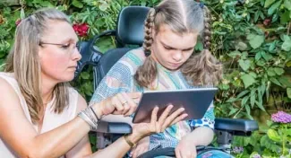 begeleidster met verstandelijk berperkt meisje in rolstoel, ze kijken samen op een tablet